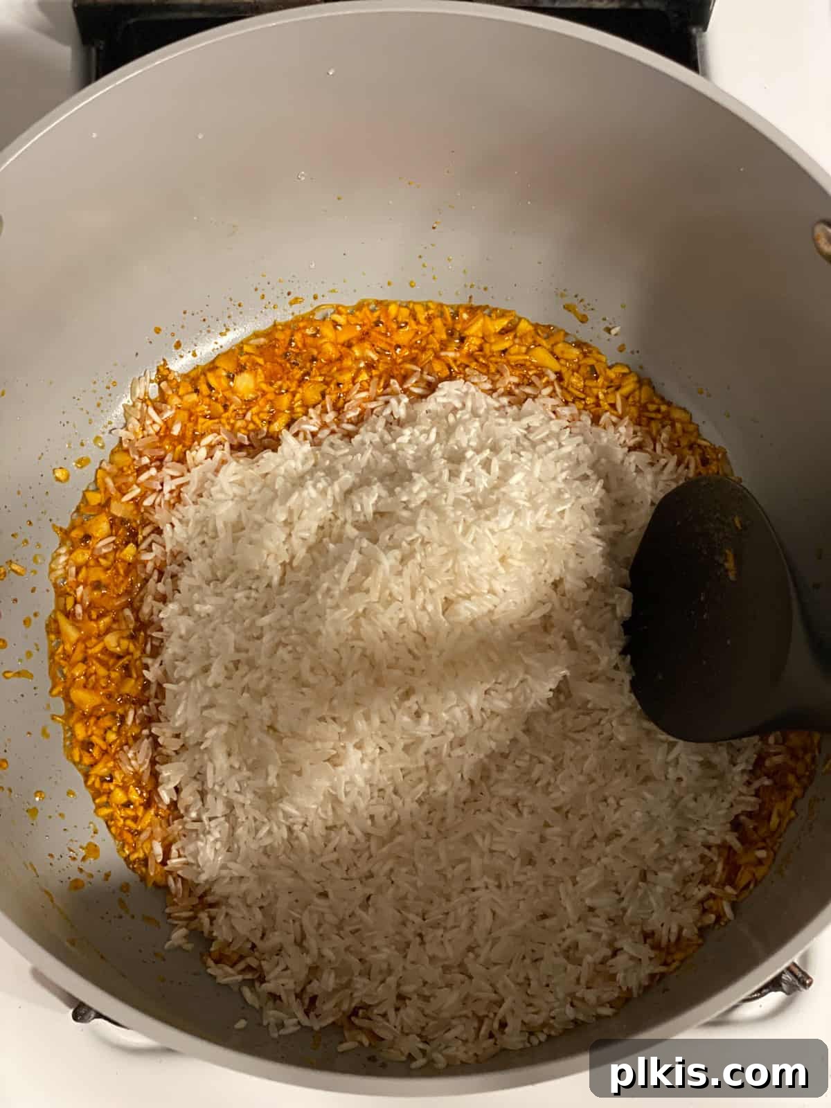 Aromatic Garlic Rice 7 Process shot of stirring rinsed long-grain white rice into the pan with oil, achiote, and garlic, ensuring each grain is coated and lightly toasted.