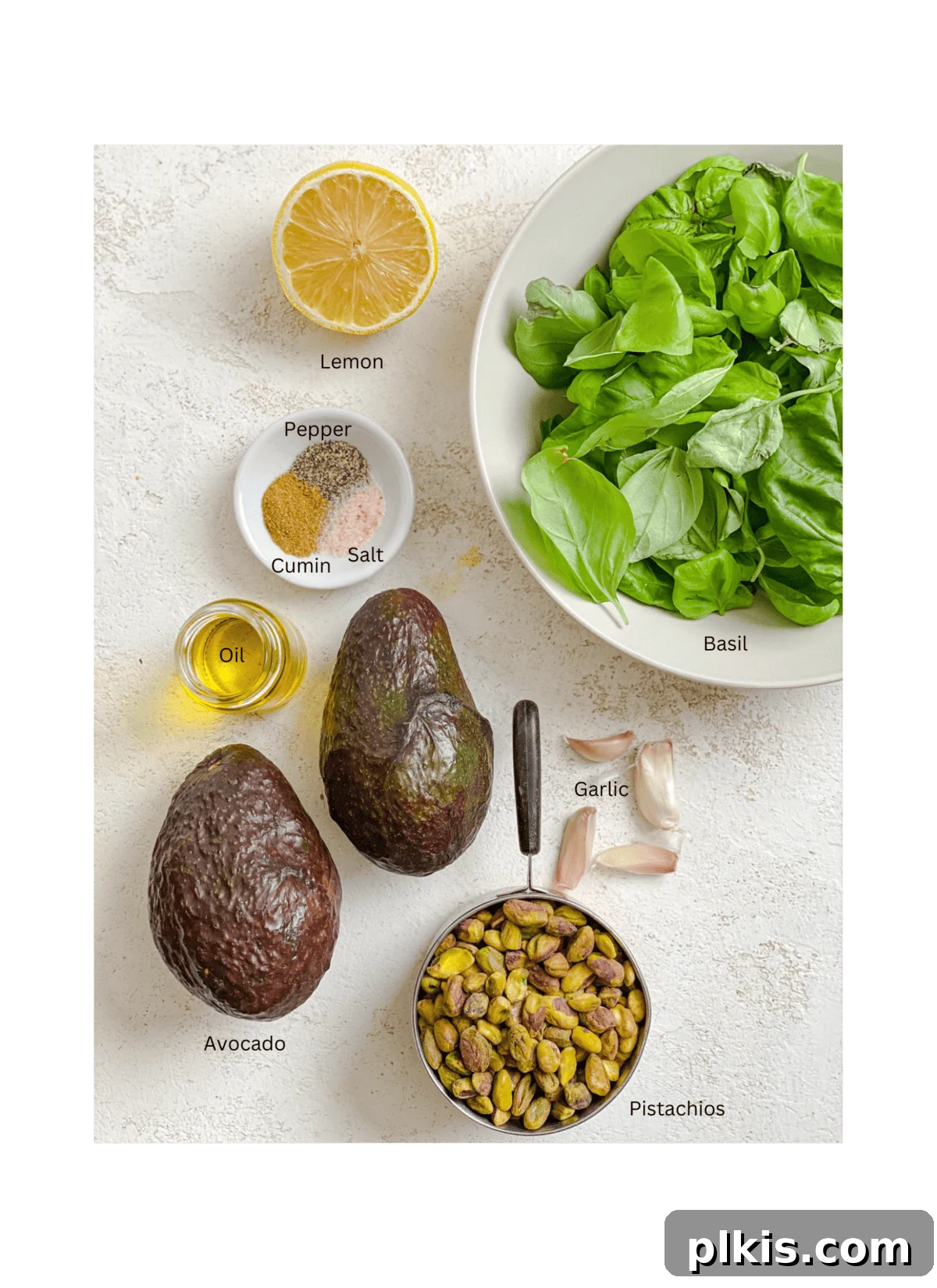Lush Avocado Pesto Pasta 3 Individual ingredients for amazing avocado pesto pasta, including fresh basil, ripe avocados, pistachios, and garlic cloves, laid out on a white surface.