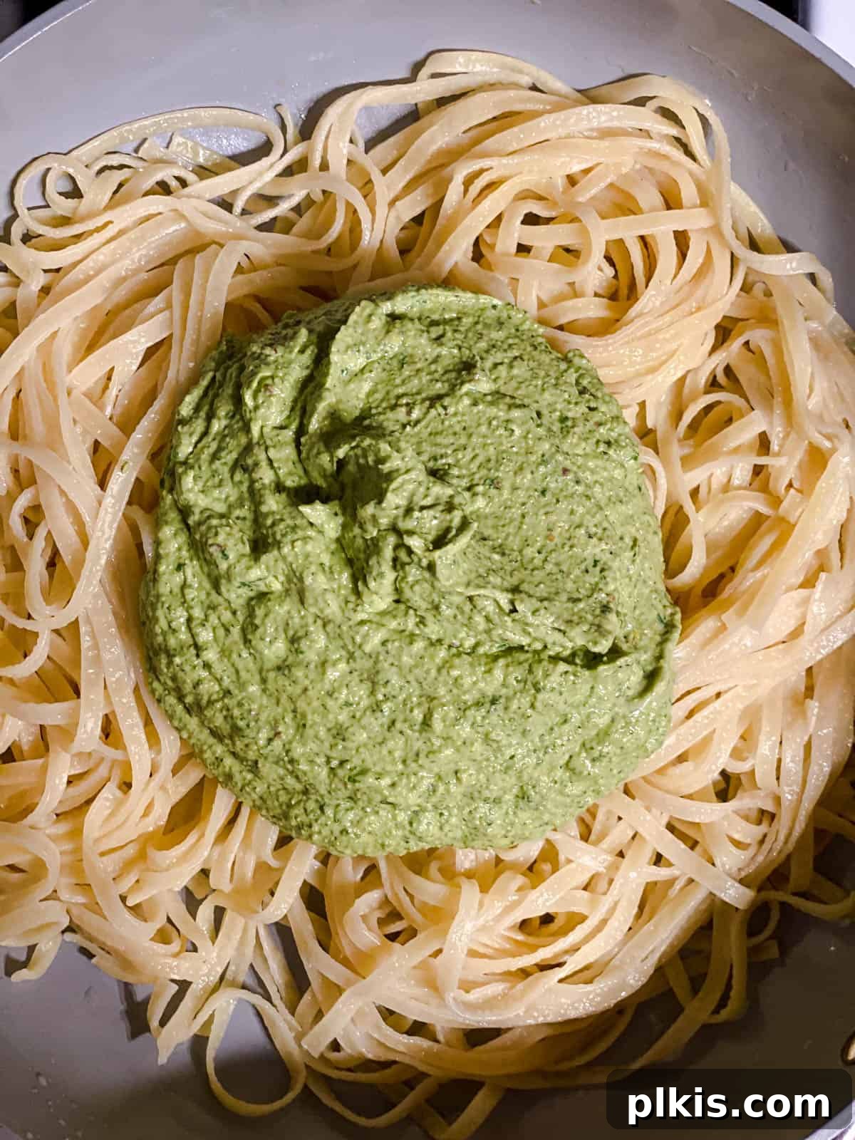 Lush Avocado Pesto Pasta 7 Cooked pasta being tossed with a generous amount of creamy avocado pesto in a large mixing bowl.