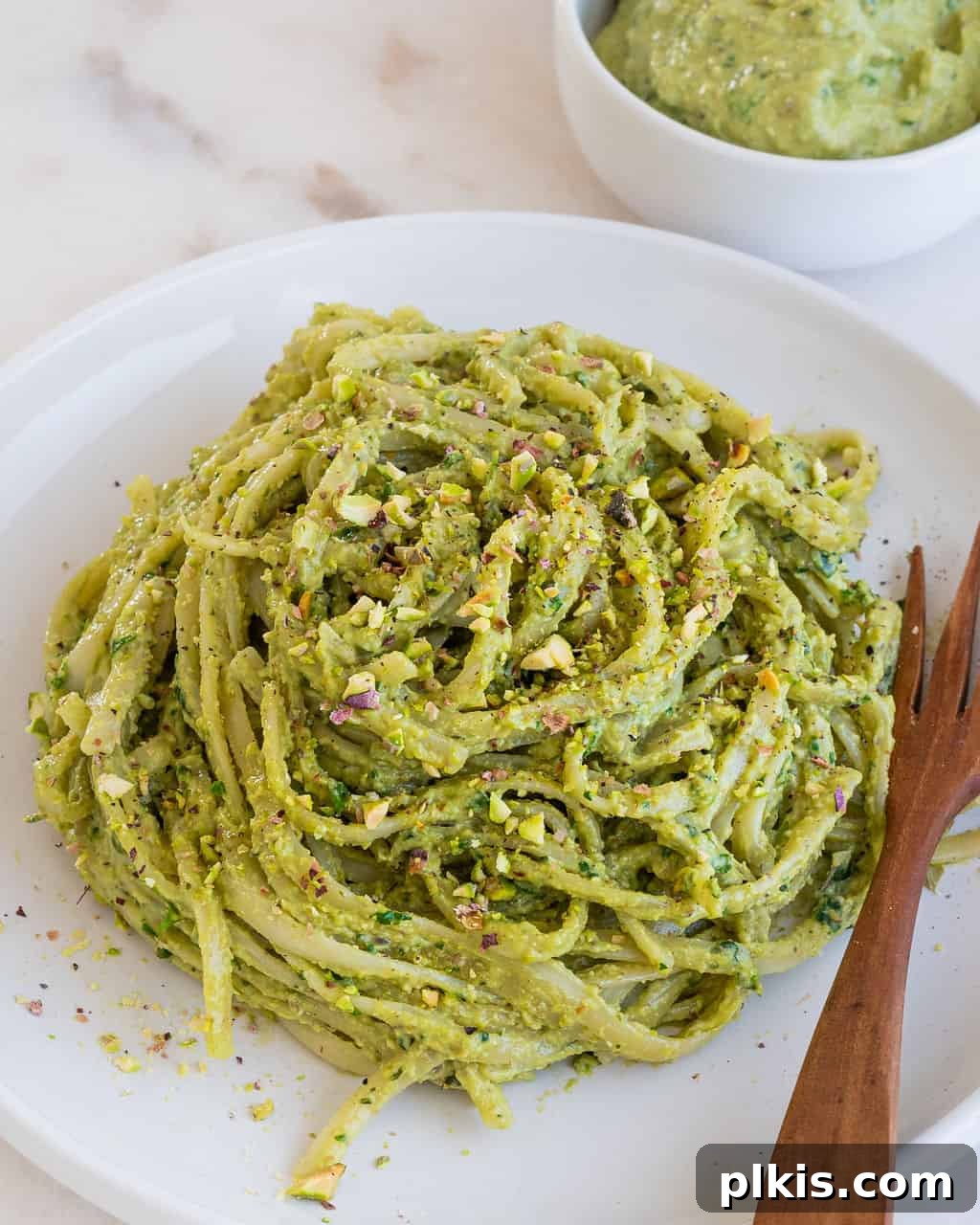 Lush Avocado Pesto Pasta 9 A serving of creamy avocado pesto in a small white bowl, garnished with fresh basil leaves, against a clean white background.