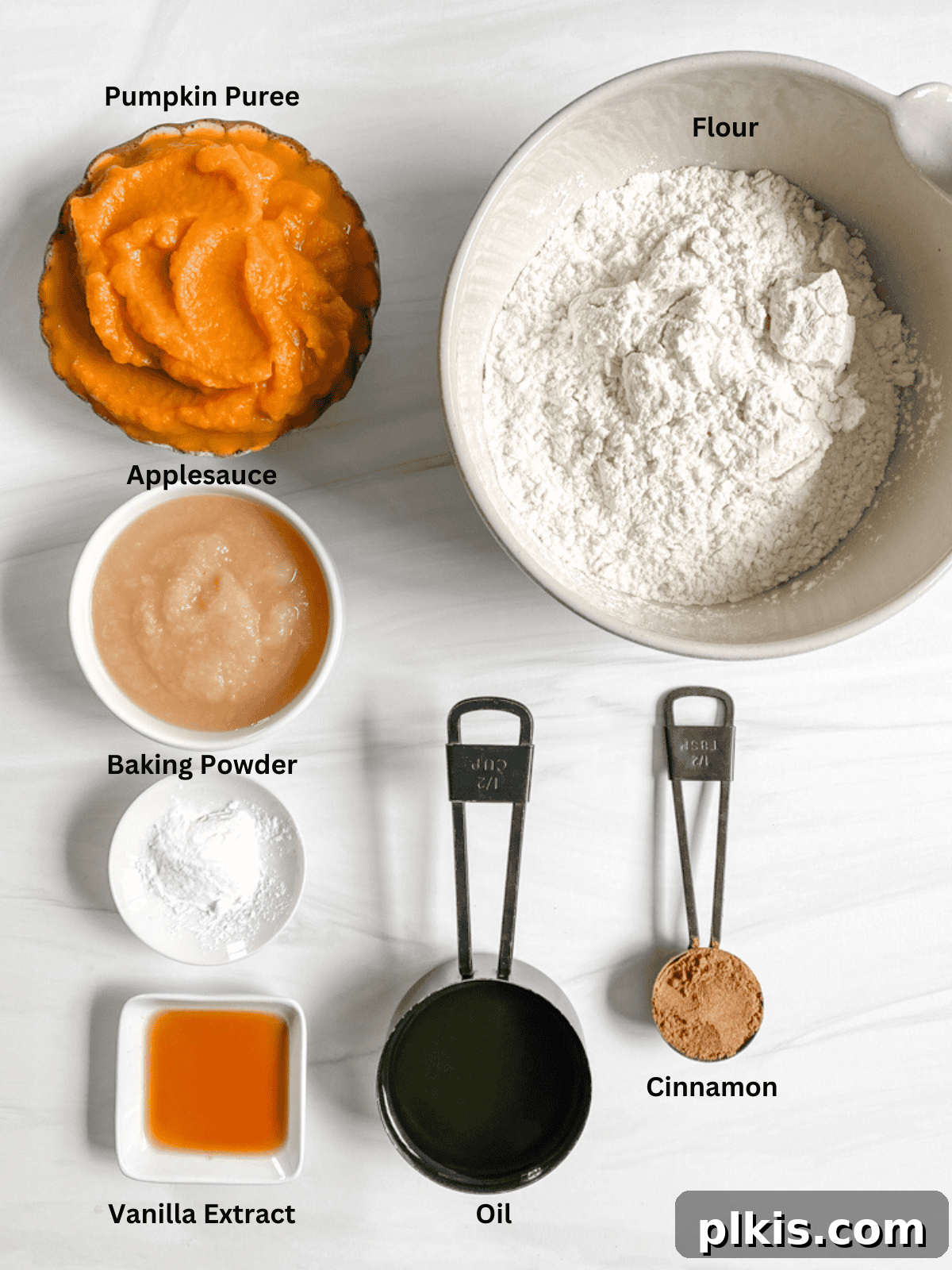 Ingredients for Vegan Pumpkin Bread measured out on a white surface, including pumpkin puree, applesauce, oil, flour, and spices.