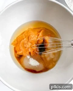Process of combining wet ingredients for pumpkin bread in a white bowl against a white background.