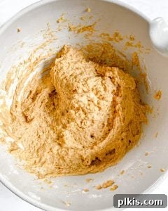 Process of mixing wet ingredients for pumpkin bread in a white bowl against a white background.