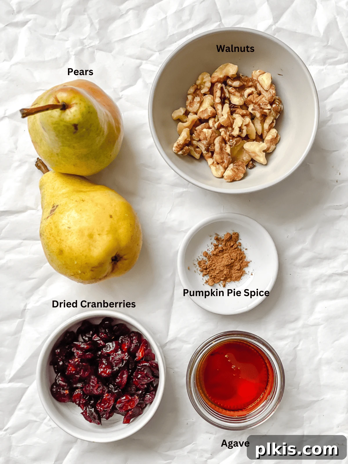 Sweet Baked Pears with Nutty Fruit Filling 3 An array of fresh pears, assorted nuts, dried fruits, and a bottle of maple syrup laid out on a white surface, showcasing the simple ingredients for this baked pear recipe.