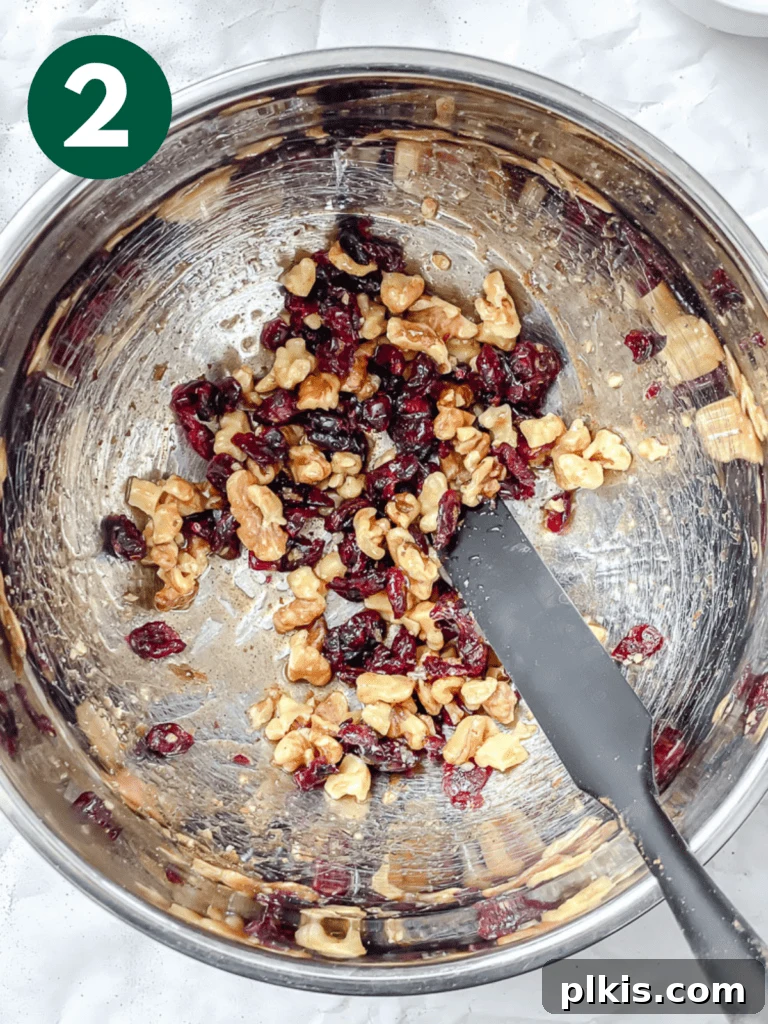Sweet Baked Pears with Nutty Fruit Filling 5 Close-up shot of hands mixing walnuts, dried cranberries, and maple syrup in a bowl, demonstrating the preparation of the pear filling.