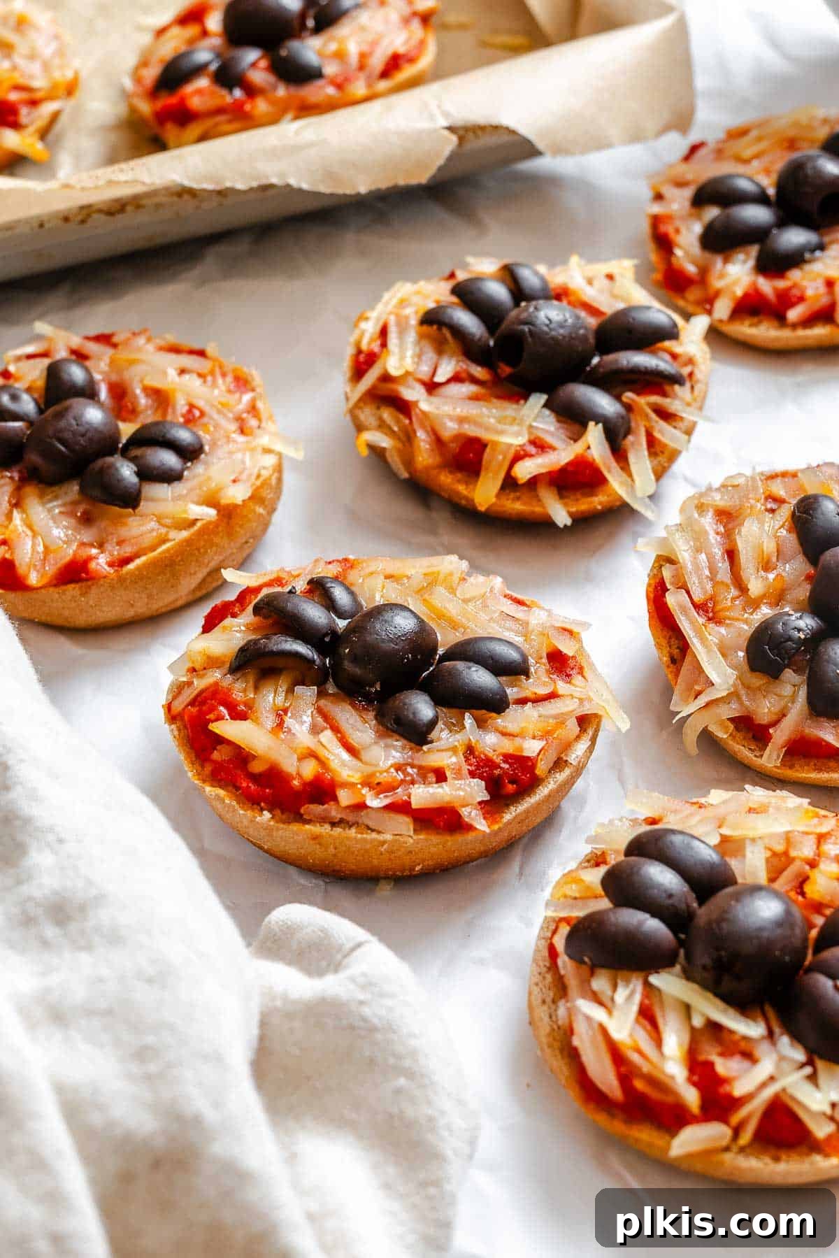 Spooky Spider Pizza Bites 2 Completed Mini Spider Pizza Bagel Bites arranged artfully on a white surface, showcasing the black olive spiders and melted vegan cheese.