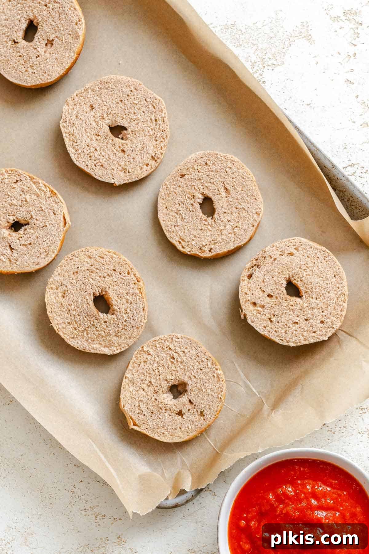 Spooky Spider Pizza Bites 4 Process shot showing sliced mini bagels arranged on a baking tray, ready for sauce and toppings.