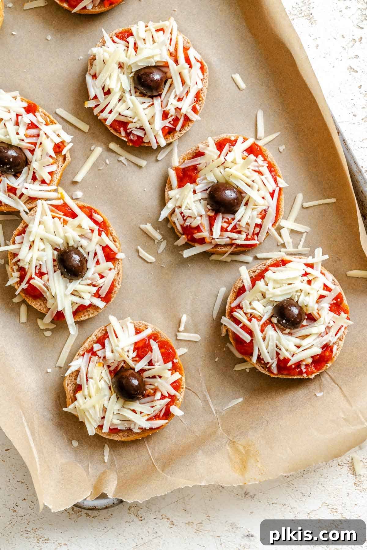 Spooky Spider Pizza Bites 5 Process shot showing mini spider pizzas with black olive bodies and legs being carefully placed on top of melted vegan cheese on bagels.