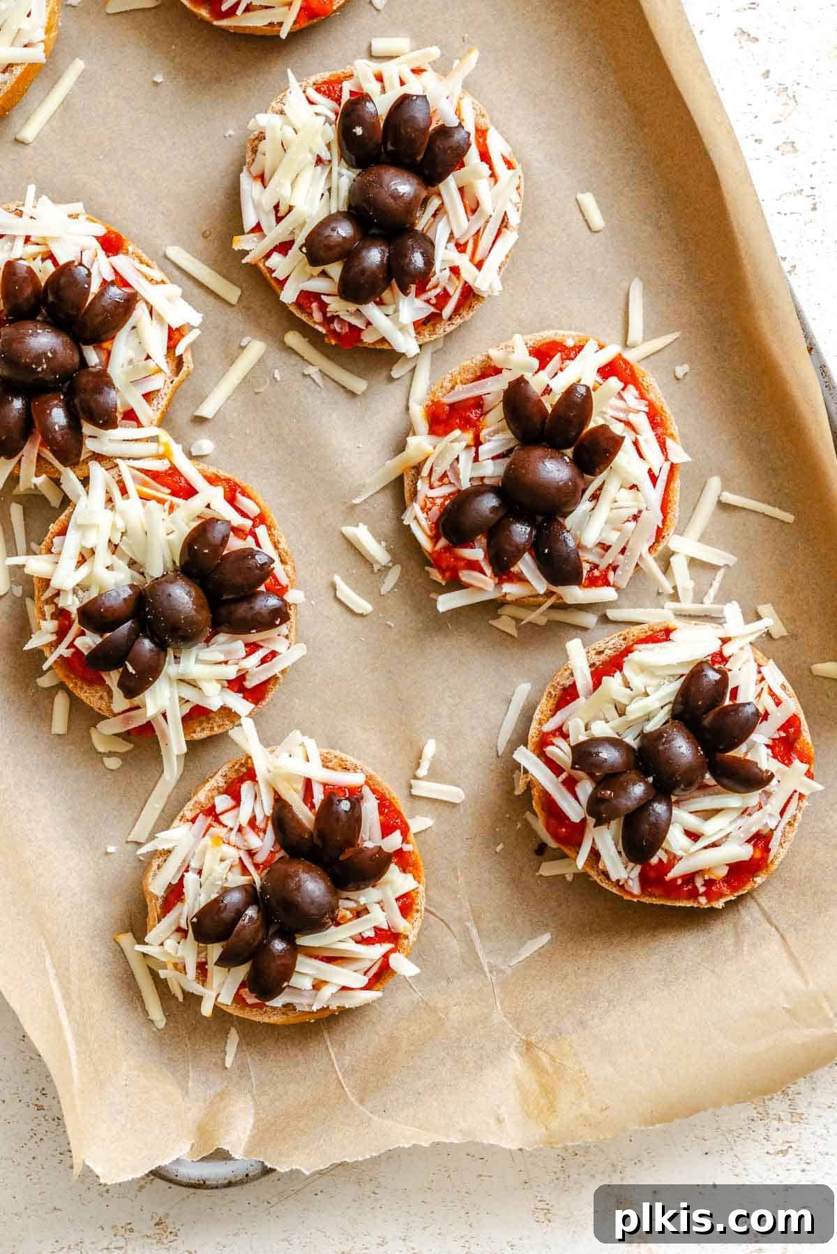 Spooky Spider Pizza Bites 6 Process shot showing unbaked Mini Spider Pizza Bagel Bites with olive spiders perfectly assembled on a baking tray, ready for the oven.