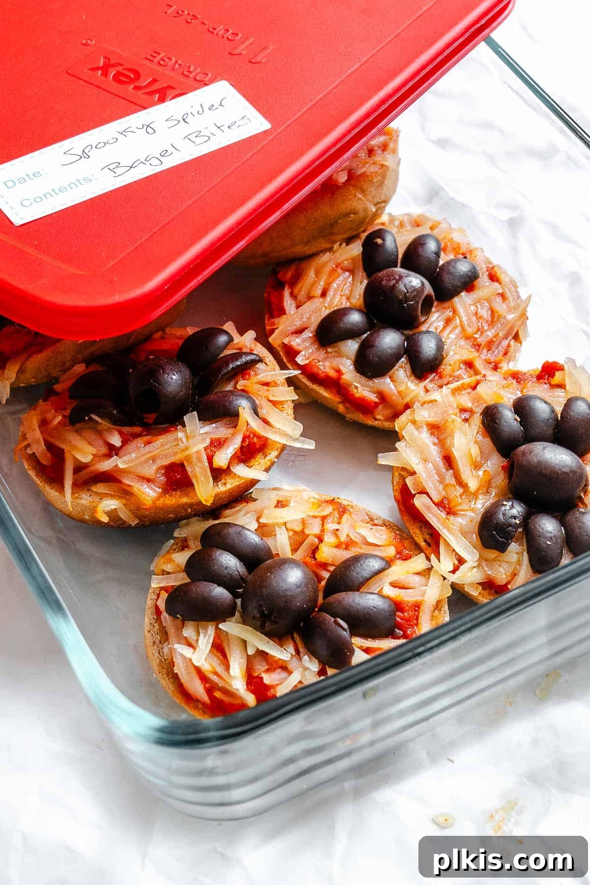 Spooky Spider Pizza Bites 9 Completed Mini Spider Pizza Bagel Bites neatly stacked in a glass storage container, ready for refrigeration.