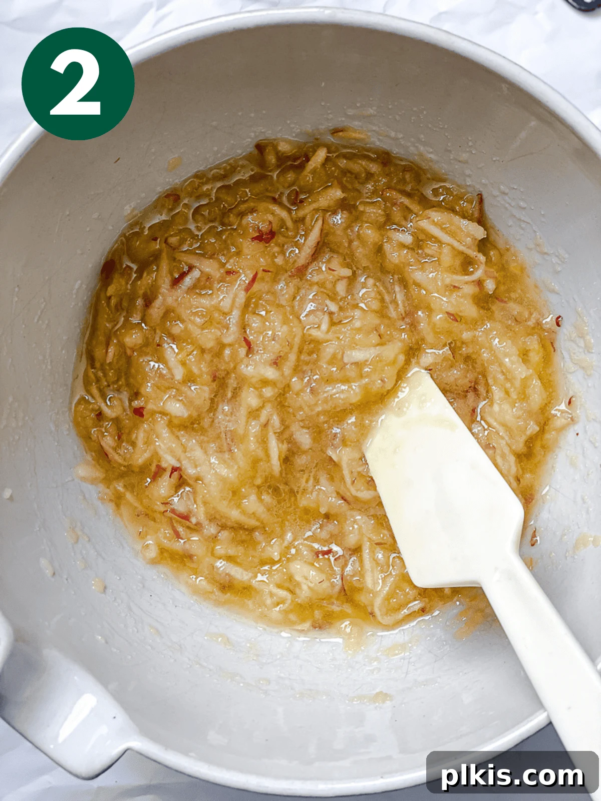 Spiced Apple Bread 5 A white spatula stirring the wet ingredients for apple cinnamon bread – applesauce, oil, sugar, grated apples, and vanilla – in a large white mixing bowl.