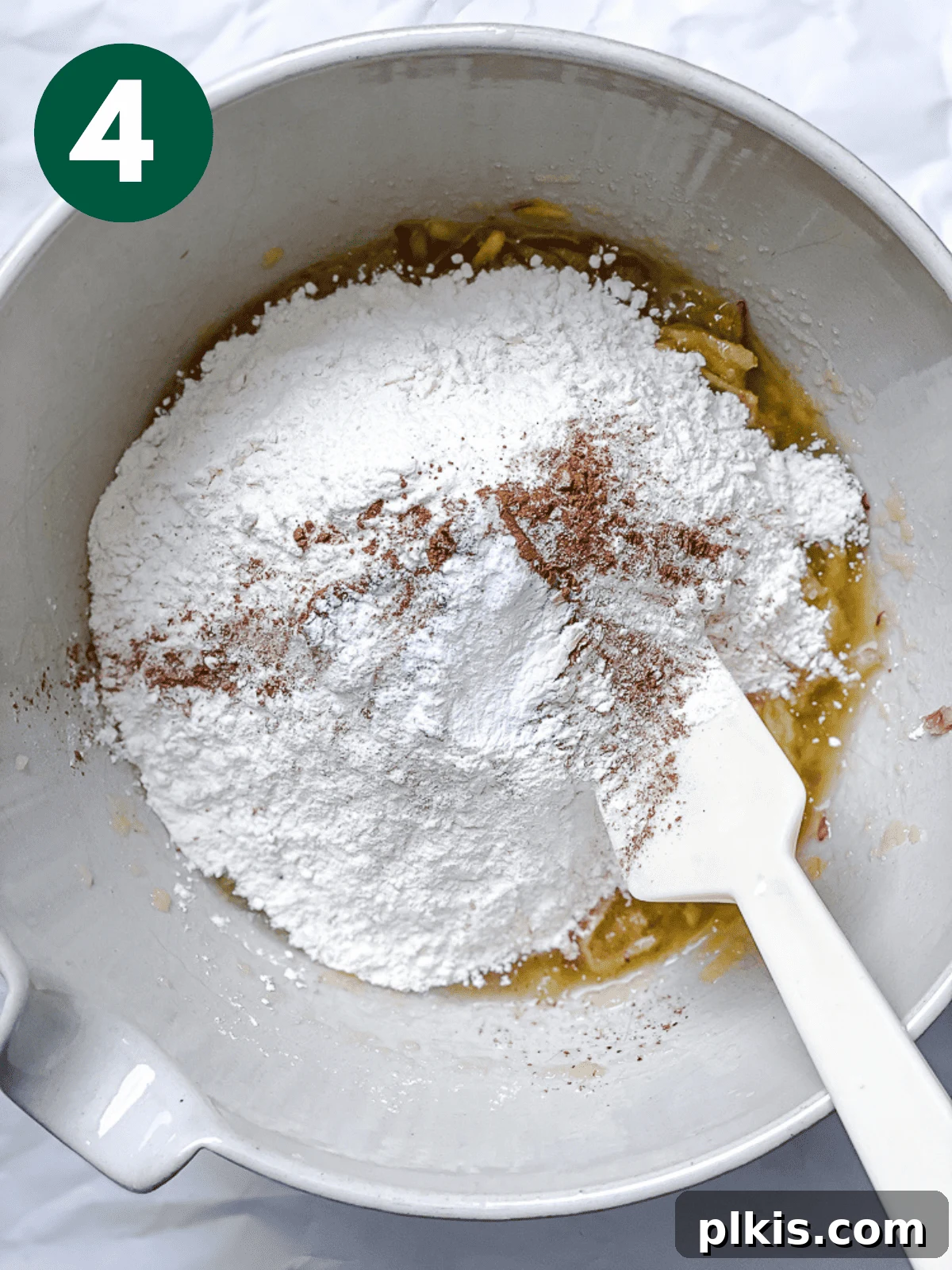 Spiced Apple Bread 7 A white spatula gently incorporating the dry ingredients—flour, salt, baking powder, and cinnamon—into the wet apple cinnamon bread batter in a large white bowl.