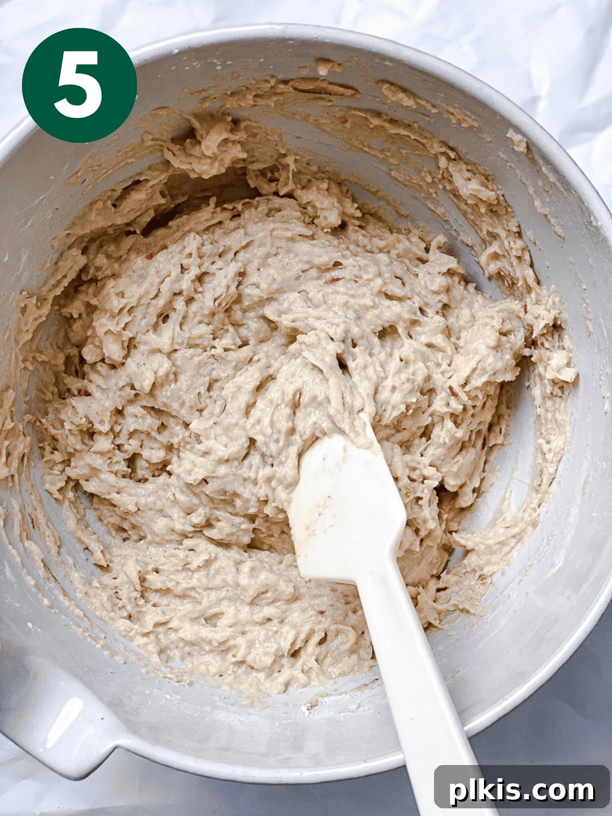 Spiced Apple Bread 8 A large white bowl containing the apple cinnamon bread batter, now fully mixed with dry ingredients, being stirred gently with a white spatula to ensure no dry pockets remain.