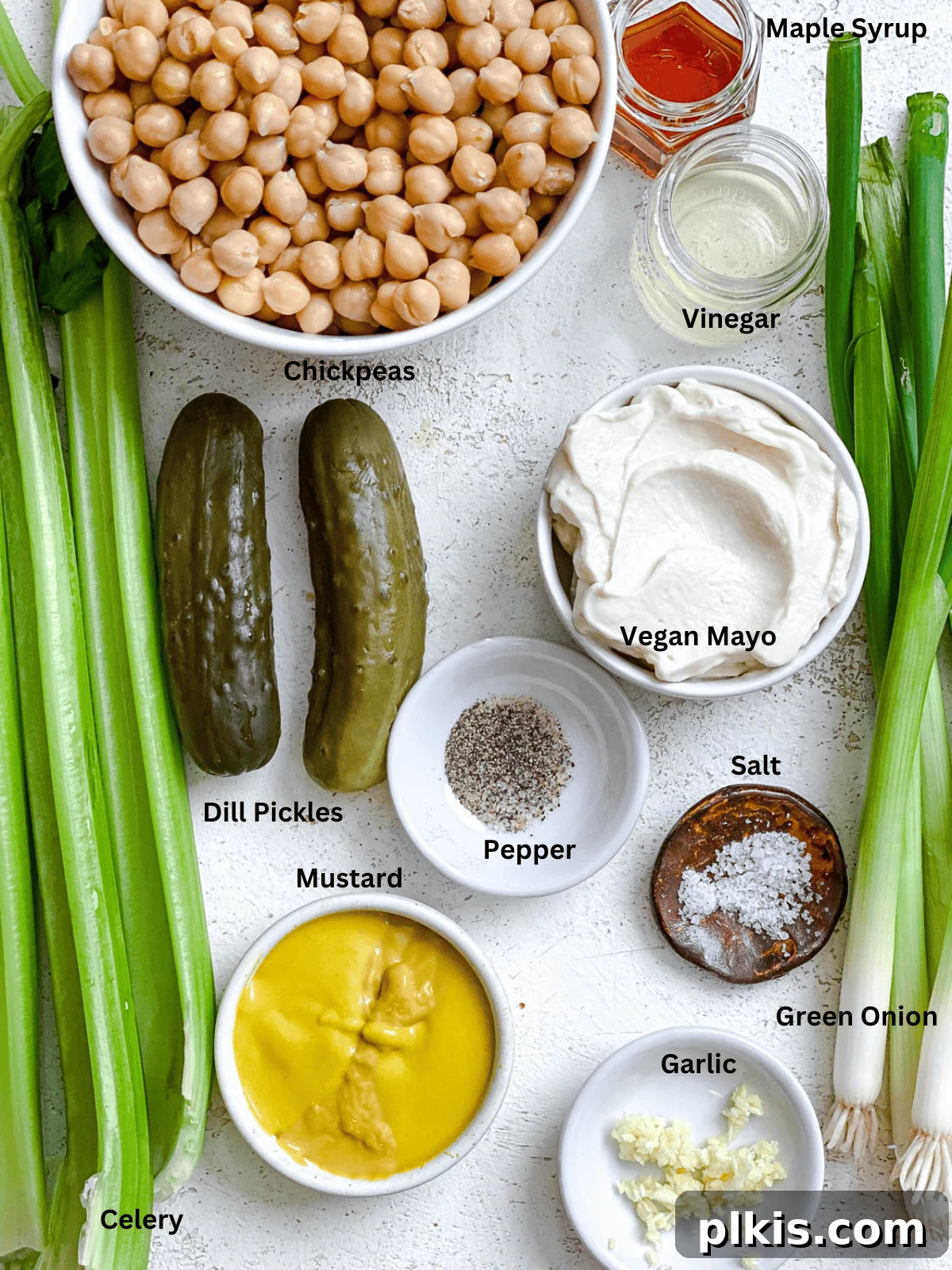 Chickpea of the Sea Salad 3 Ingredients for Plant-Based Chickpea Tuna Salad measured out on a white surface, including canned chickpeas, celery, dill pickles, green onions, vegan mayo, mustard, garlic, salt, sugar, and apple cider vinegar.