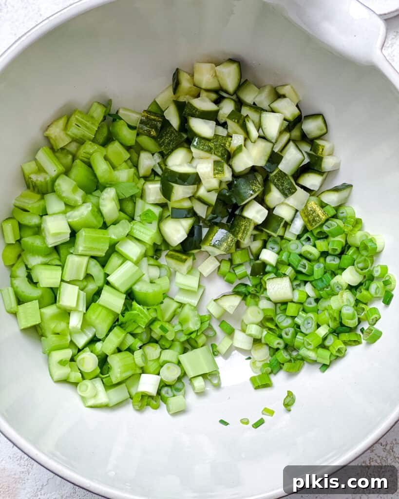 Chickpea of the Sea Salad 5 Process shot of diced celery, green onions, and pickles being added to a bowl with mashed chickpeas.