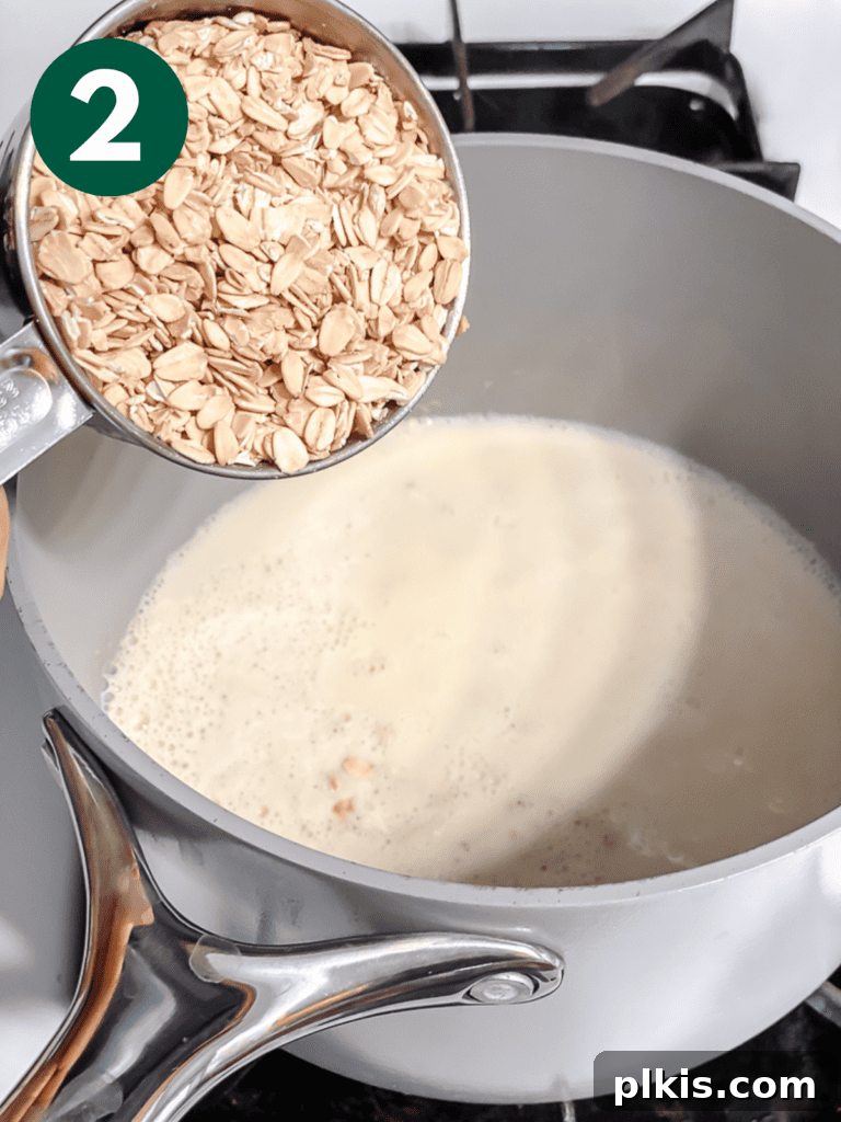 Mastering Stove-Top Oatmeal: Perfect Consistency and Delicious Variations 5 Process shot of dry oats being added to boiling plant-based milk in a saucepan.