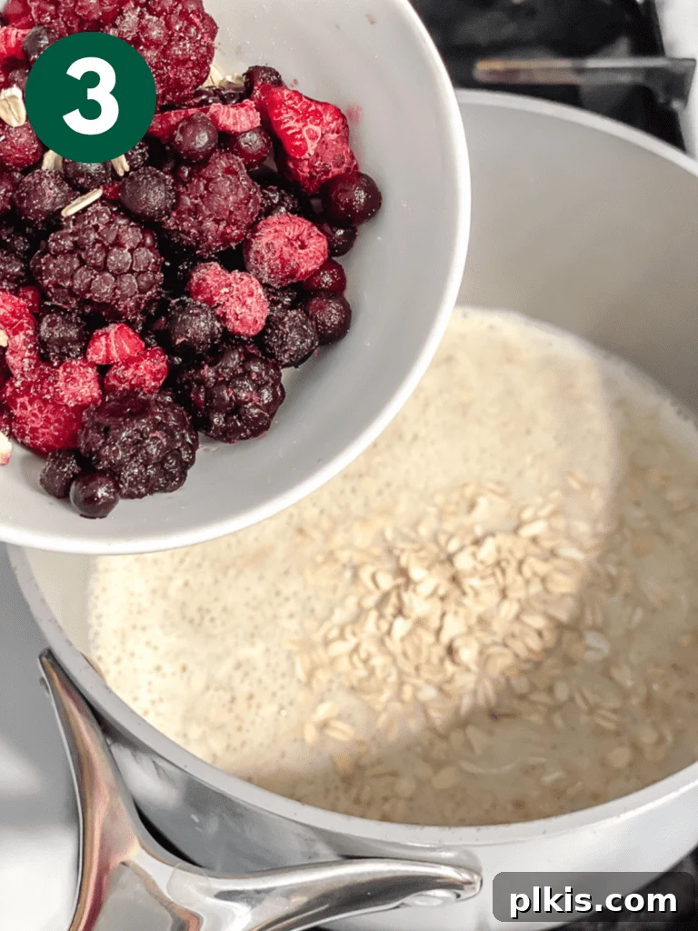 Mastering Stove-Top Oatmeal: Perfect Consistency and Delicious Variations 6 Process shot showing frozen berries being stirred into the cooking oatmeal in the saucepan.