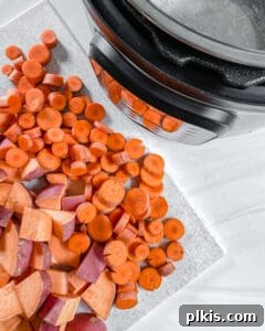 Raw, diced yams and sliced carrots placed into a pressure cooker basket with the pot in the background