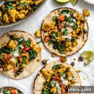 completed Vegan Breakfast Tacos on a white surface alongside pan of filling
