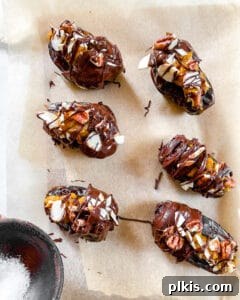 Six pumpkin-stuffed dates with chocolate coating and toppings, arranged on parchment paper before freezing.