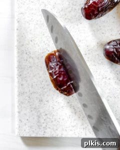 Close-up process shot of a single Medjool date being carefully sliced lengthwise with a knife.