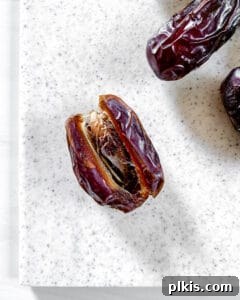 Process image displaying a single Medjool date already sliced open on a white cutting board, revealing the natural pocket.