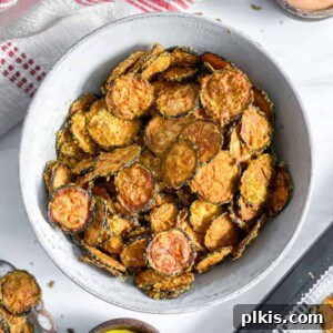 cooked zucchini chip sin a white bowl with zucchini chips in the background