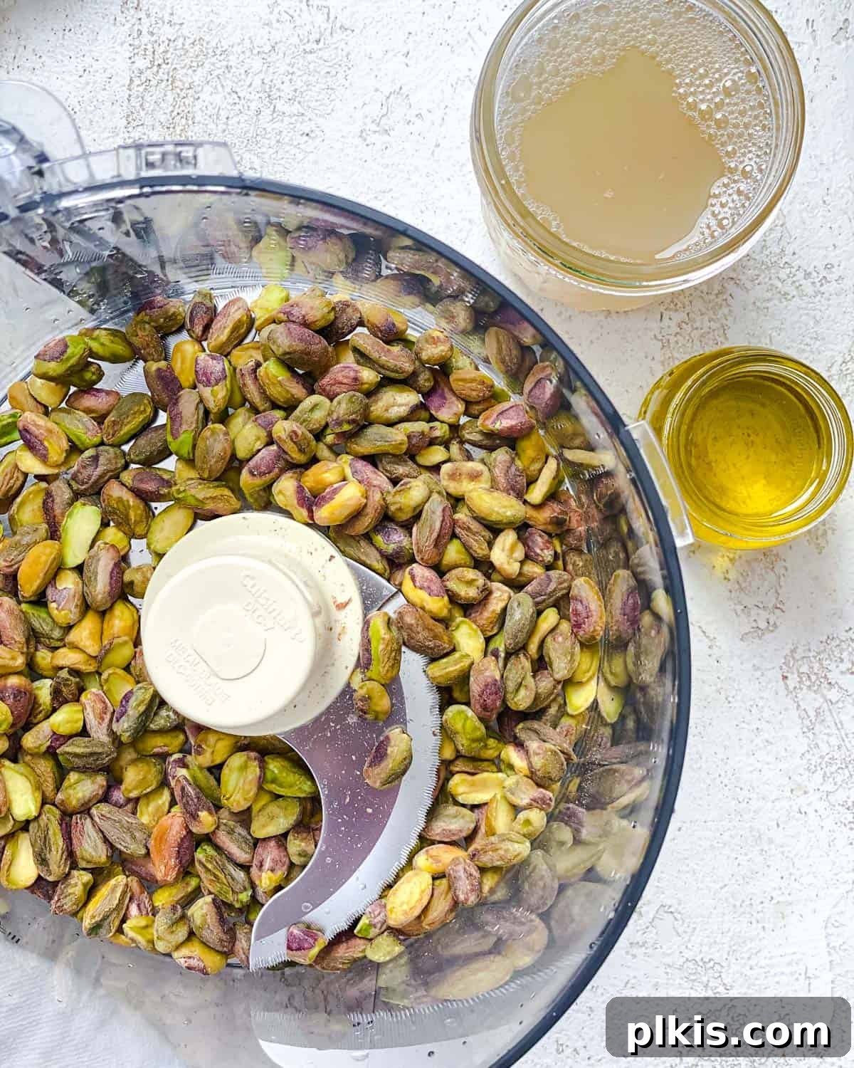 Emerald Pistachio Hummus 3 Process shot: Pistachios, olive oil, and chickpea liquid being added to a food processor.