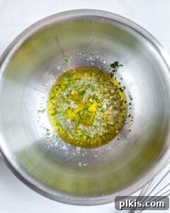 Oil and fresh herbs in a stainless steel mixing bowl, ready for vinaigrette preparation