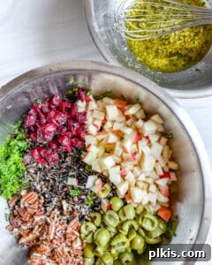 Two stainless steel bowls, one with wet ingredients for dressing, one with dry salad ingredients, on a white background