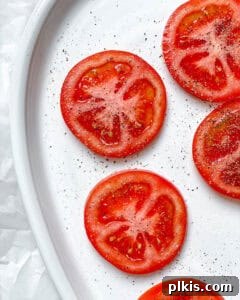 Plant-Based Caprese Delight 8 Sliced tomatoes on a white plate, seasoned