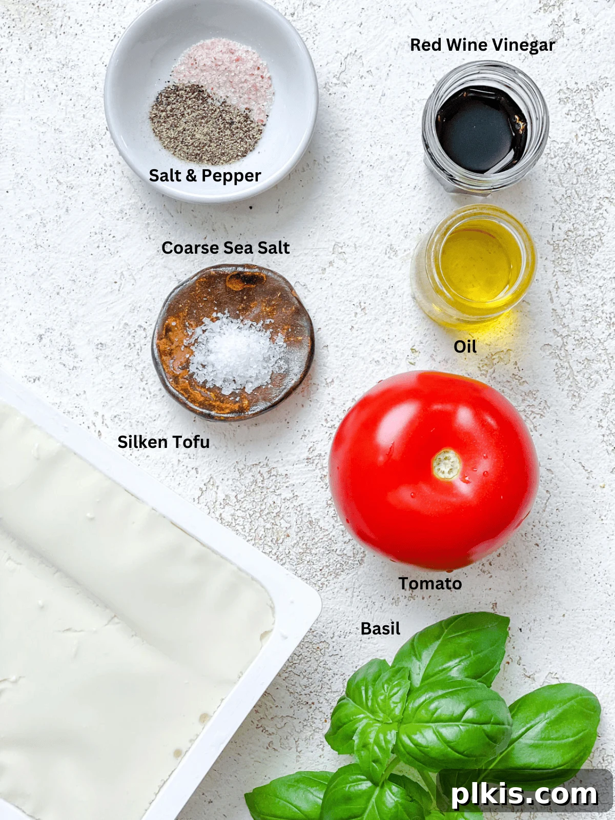 Plant-Based Caprese Delight 3 Fresh ingredients for Vegan Caprese Salad, including ripe tomatoes, silken tofu, and fresh basil leaves, on a white surface.