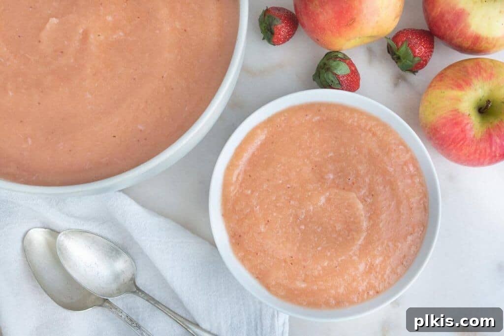 20 Delicious Vegan Autumn Desserts 17 finished strawberry apple sauce in a white bowl with apples and utensils on the side against a white background