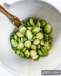 Crispy Air Fryer Brussels Sprouts 10 brussels sprouts in a white bowl with a wooden spoon with ingredients being mixed