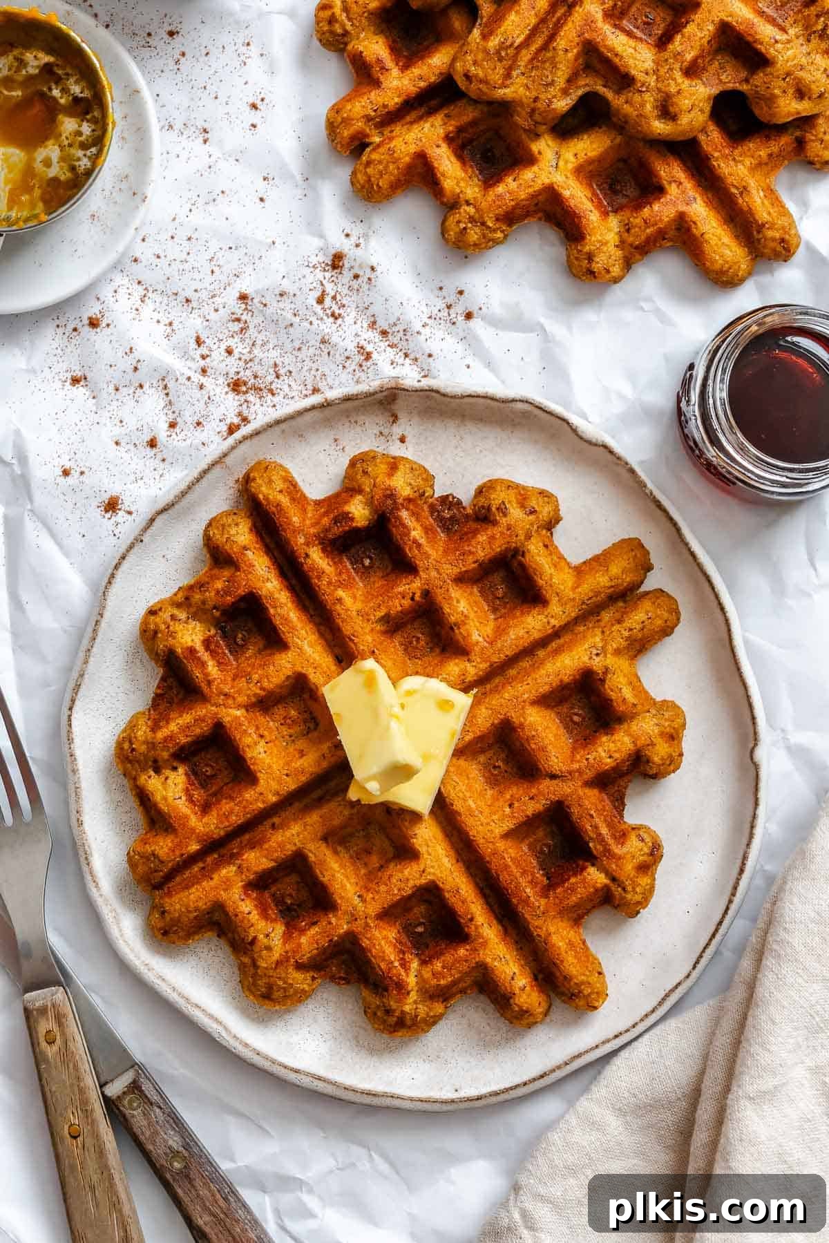 Plant-Based Pumpkin Patch Waffles 2 A stack of perfectly golden-brown Vegan Pumpkin Waffles on a plate, garnished with a sprinkle of powdered sugar and a drizzle of maple syrup.