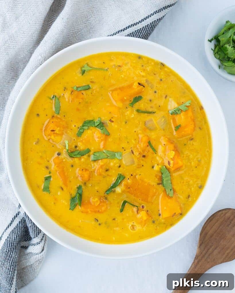 45 Mouthwatering Vegan Thanksgiving Recipes 11 A comforting bowl of finished curried butternut squash lentil soup, with a kitchen towel and ingredients in the background.