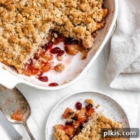 45 Mouthwatering Vegan Thanksgiving Recipes 75 Completed Apple Cranberry Crisp with a piece plated on a small white plate against a white background.