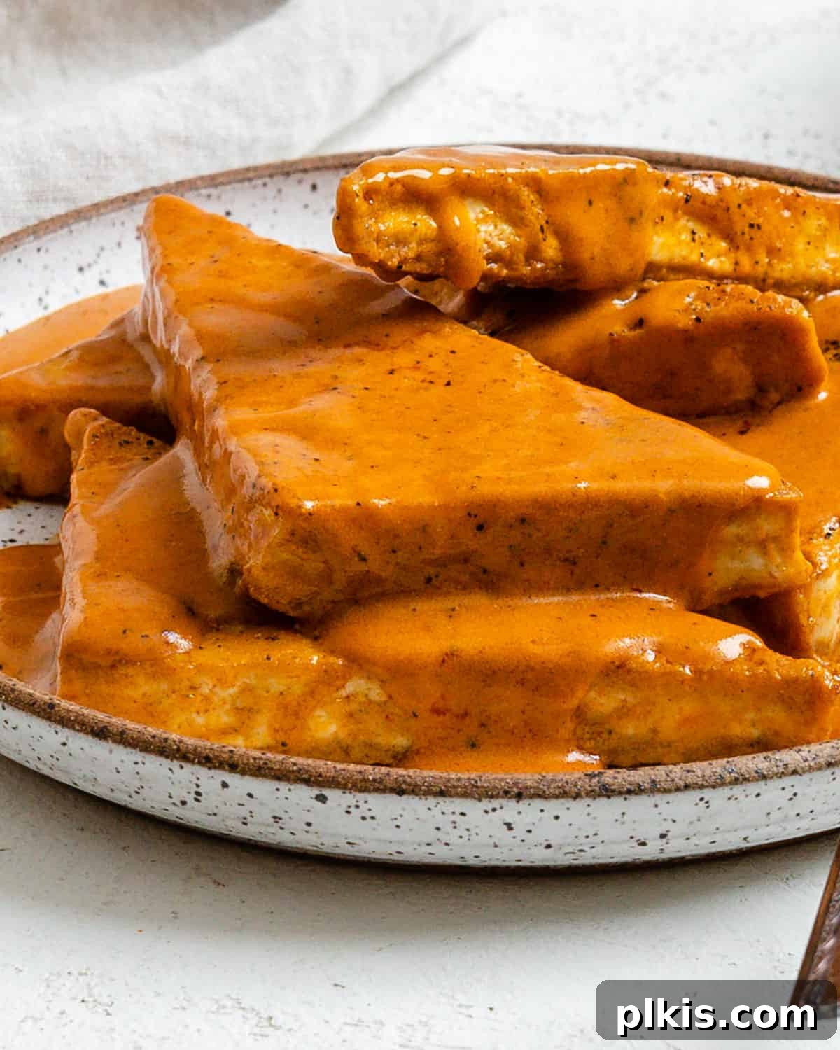 Buffalo Tofu Your Way: Easy Fried, Baked, or Air-Fried 12 Close-up of completed Easy Buffalo Tofu plated on a white dish, garnished with fresh herbs