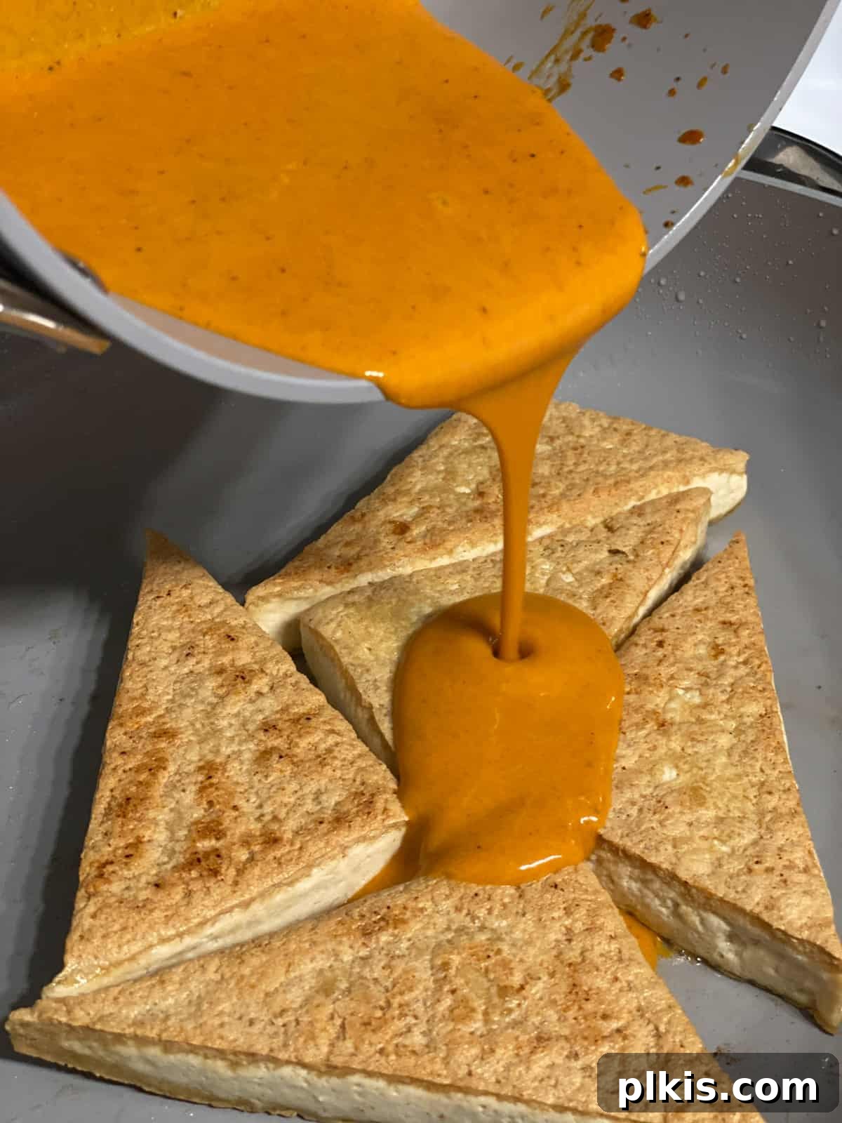 Buffalo Tofu Your Way: Easy Fried, Baked, or Air-Fried 10 Process shot of adding buffalo sauce to crispy tofu wedges in the pan
