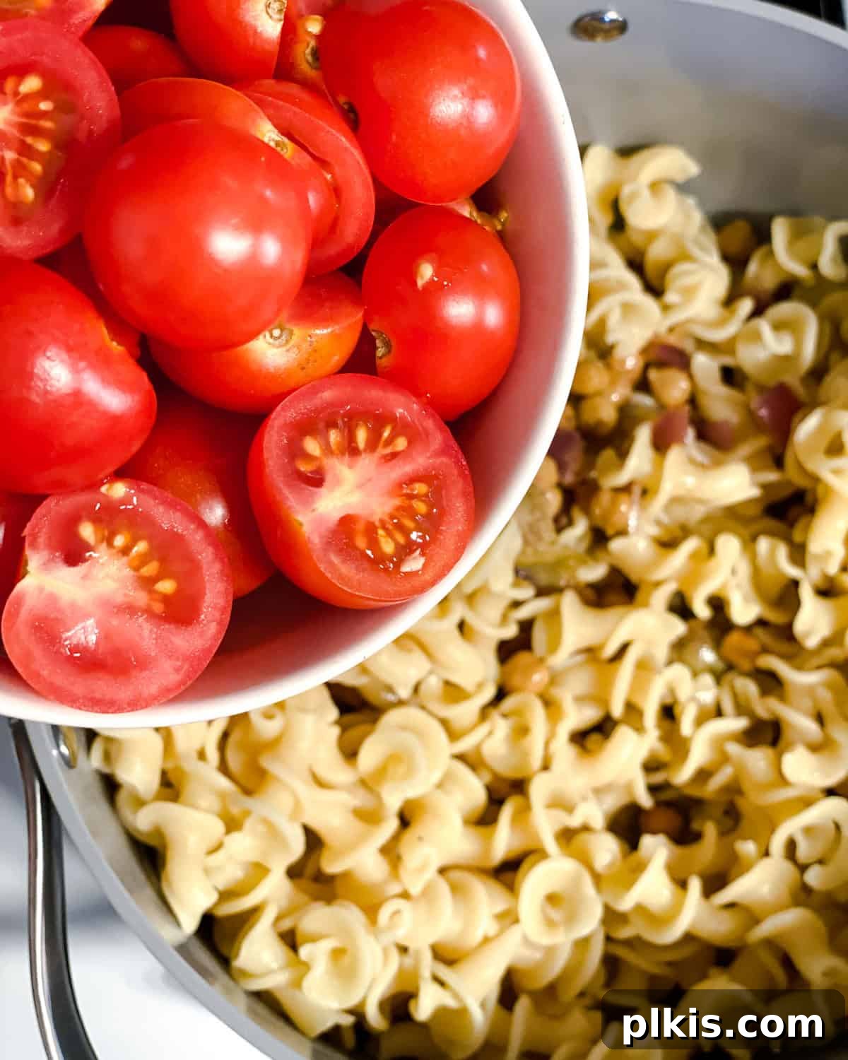 Refreshing Summer Pasta Salad 7 Process shot of adding fresh cherry tomatoes to the finished pasta salad mixture.