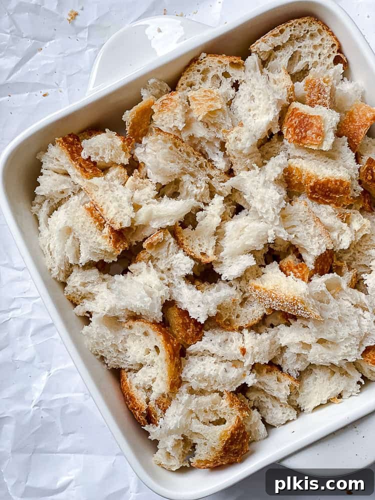 Decadent Vegan Bread Pudding 4 Process shot showing torn bread chunks evenly distributed in an 8-inch square baking dish.