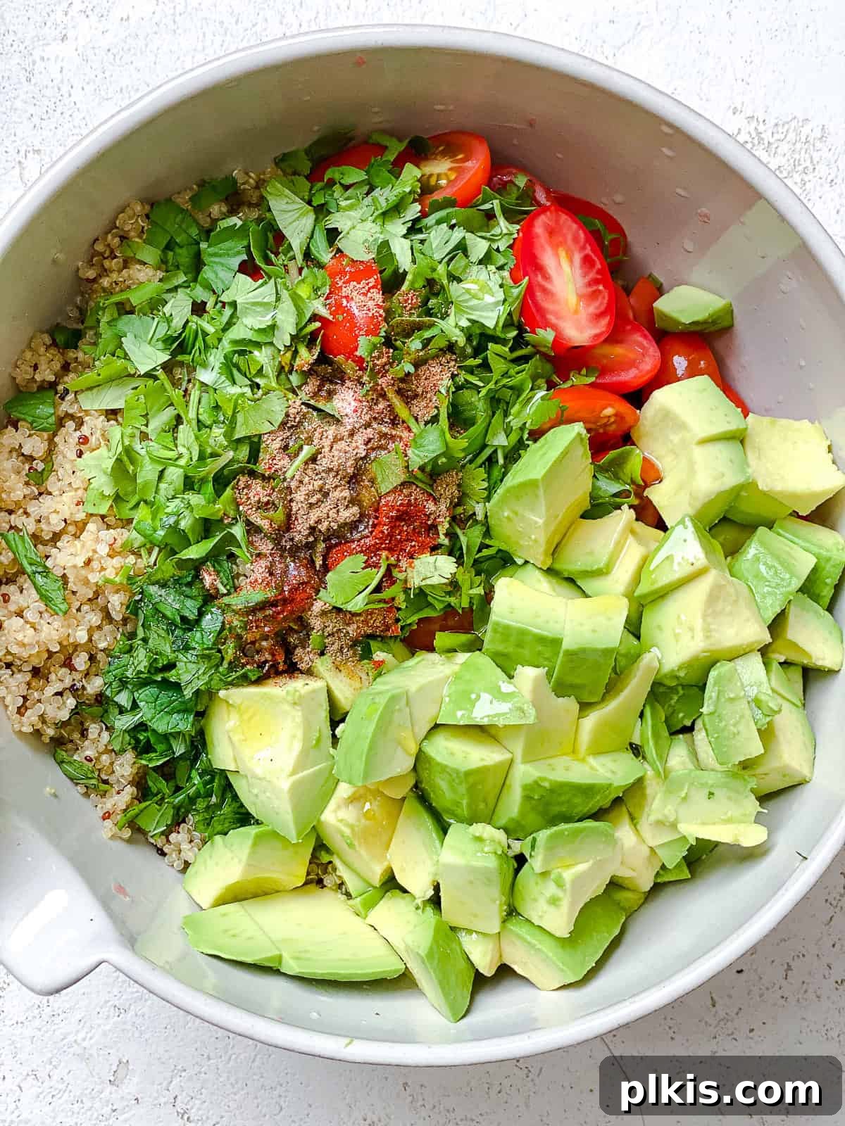 Process shot showing all the fresh ingredients, including grapefruit, avocado, quinoa, and herbs, being combined in a large bowl.