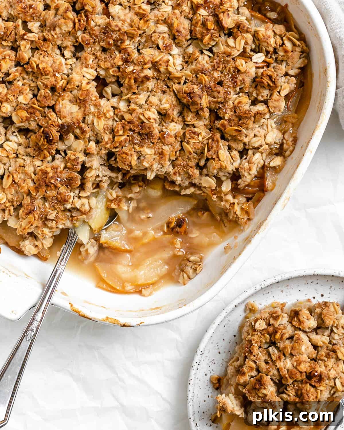 A golden-brown Easy Pear Crisp [Vegan Pear Crumble] in a rustic baking tray, with a single, perfectly portioned piece on a white plate beside it, ready to be served.