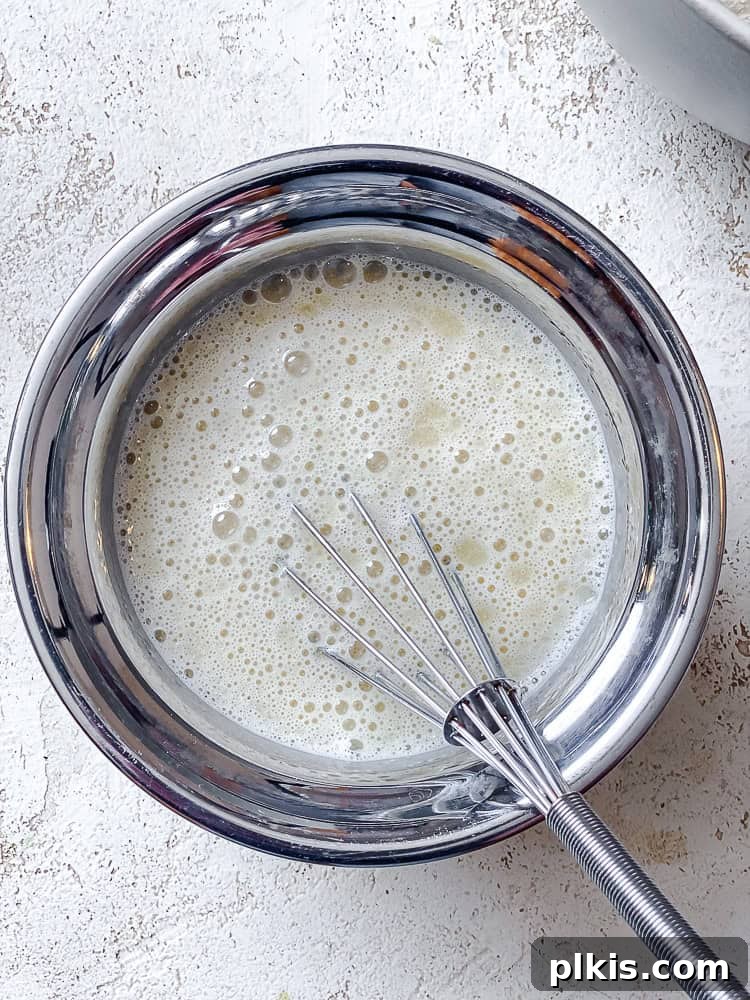 Plant-Based Waffles 5 A medium bowl showcasing plant-based milk, vegetable oil, and vanilla extract being whisked together until well combined, forming the wet ingredients for the waffle batter.