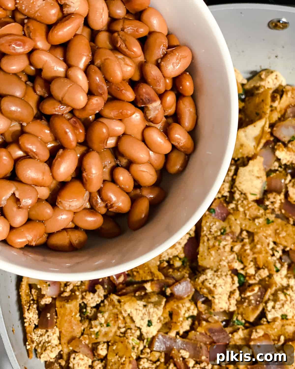 Vegan Chilaquiles Red or Green 11 Process shot of adding pinto beans to the pan, ready to be mixed with the rest of the chilaquiles ingredients.