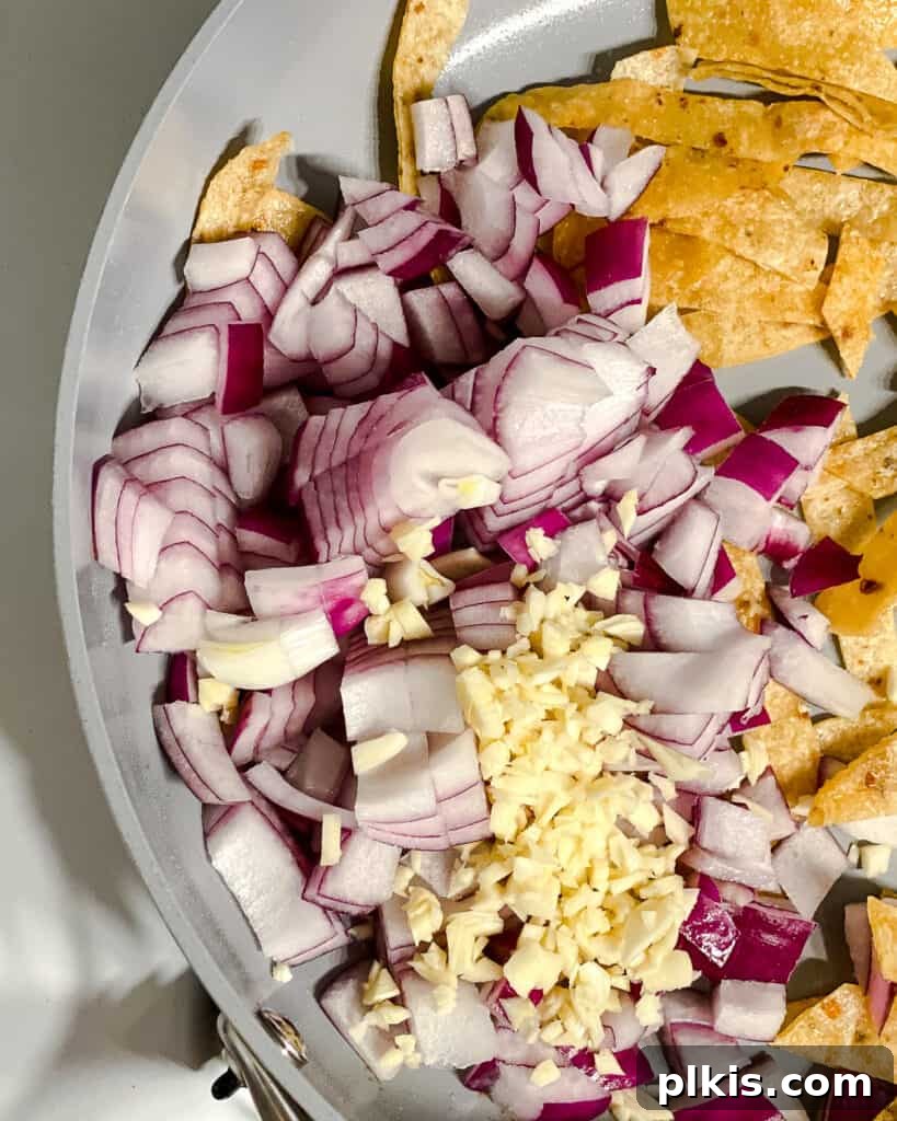 Vegan Chilaquiles Red or Green 7 Process shot of adding diced onions and minced garlic to the pan with the crispy tortilla strips, ready for sautéing.