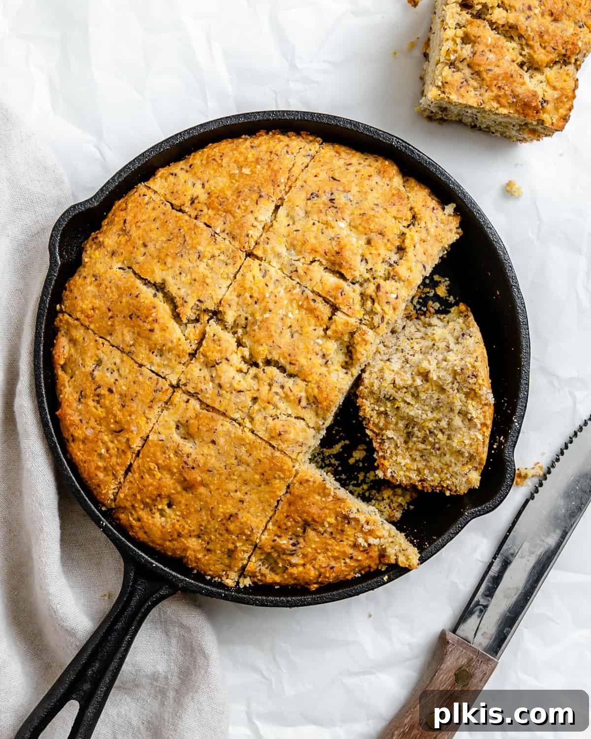 Golden Crust Vegan Cornbread in a Cast Iron Skillet 2 completed Vegan Cornbread Recipe in a Cast Iron Skillet against a white background, garnished with a sprig of rosemary.