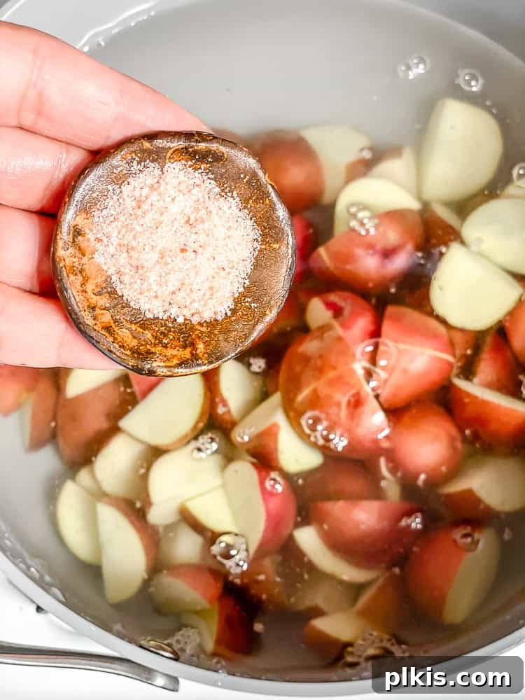 Process shot showing pouring salt into a pot with water and chopped red baby potatoes.