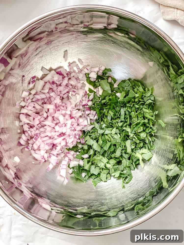 Process shot showing chopped red onion and parsley in a metal bowl.