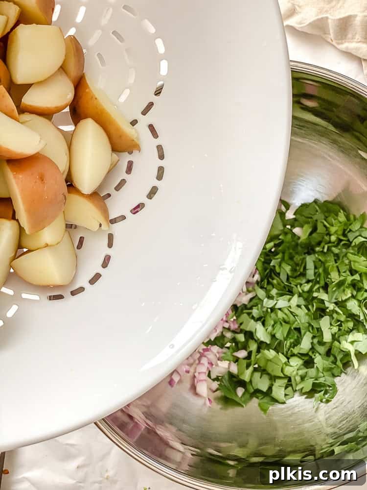 Process shot showing pouring cooked potatoes into a metal bowl with chopped red onion and parsley.